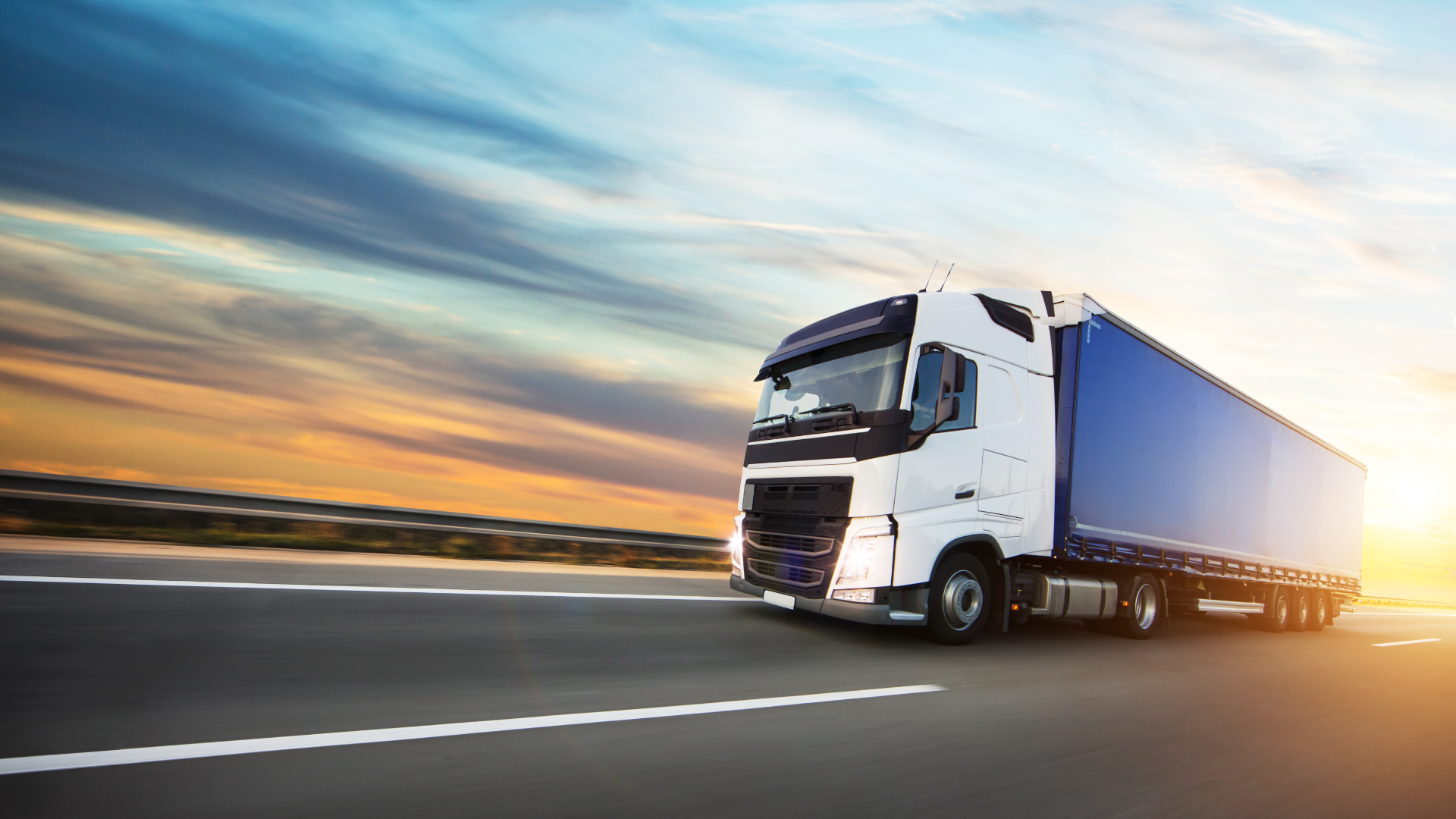 artic lorry driving on a road during sunset